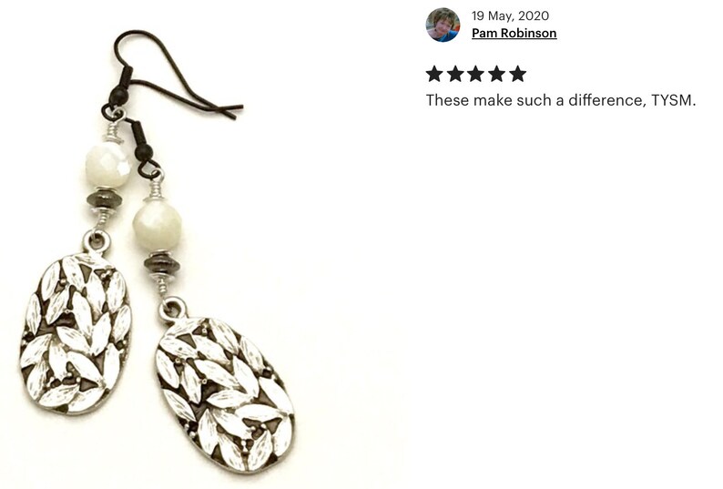 May include: Silver earrings with white oval beads and a leaf design. The earrings have a hook closure.