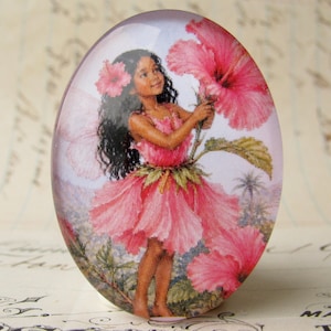 May include: Oval-shaped glass paperweight featuring a young girl in a pink floral dress, holding a large pink hibiscus flower. The girl has dark hair and is set against a tropical landscape with palm trees.