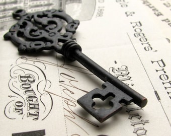 May include: A black metal skeleton key with an ornate design on the top and a clover-shaped keyhole. The key is lying on a piece of paper with the text "Bought of" and "Rogers, Prentice & Co." printed on it.