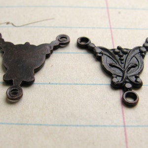 May include: Two antique bronze metal connector charms with three loops. One charm is plain and the other has a floral design.