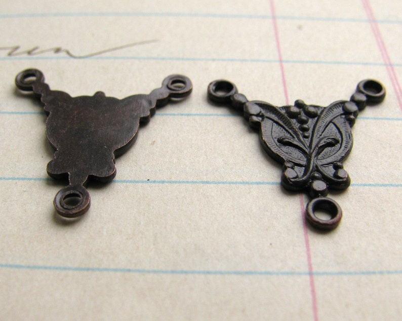May include: Two antique bronze metal connector charms with three loops. One charm is plain and the other has a floral design.