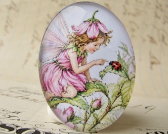 May include: An oval glass cabochon featuring a detailed illustration of a fairy with light brown hair, wearing a pink dress and a flower hat, sitting on green leaves and reaching out to touch a small red and black ladybug on a leaf.