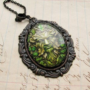 Puede incluir: Un collar con un colgante de bronce con un camafeo de vidrio verde y marr&oacute;n que presenta un rostro de hombre verde rodeado de hojas.