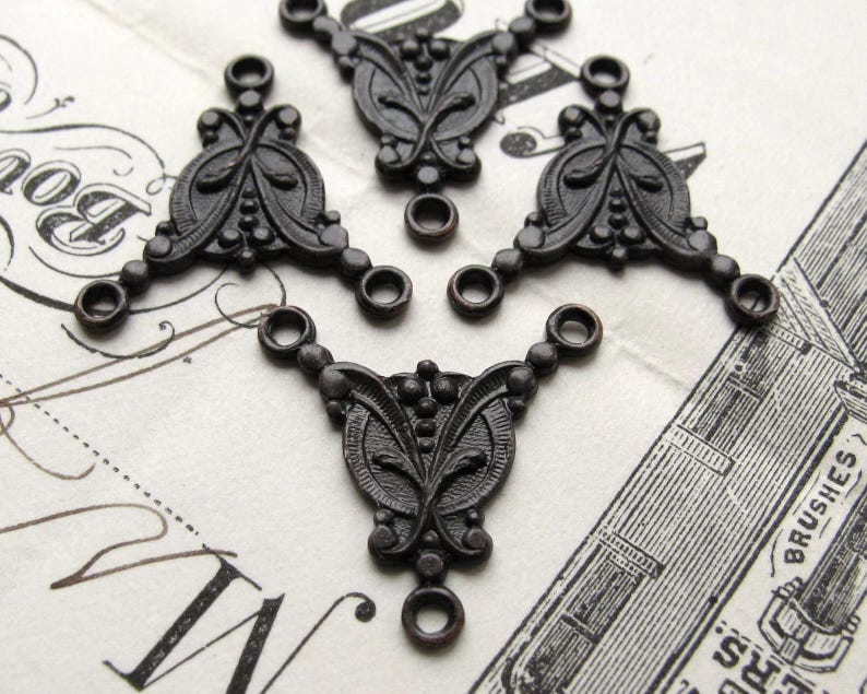 May include: A set of three black metal decorative embellishments with a floral design. Each embellishment has three loops for attaching to a project.