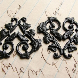 May include: Two black metal decorative embellishments with a floral design. The embellishments are in the shape of a heart and a triangle.