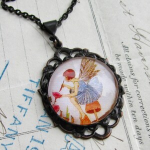 May include: A copper-toned pendant necklace with a glass cameo featuring a fairy with blue wings sitting on a mushroom. The fairy is holding a flower and is surrounded by other mushrooms and greenery. The cameo is set in a filigree frame.