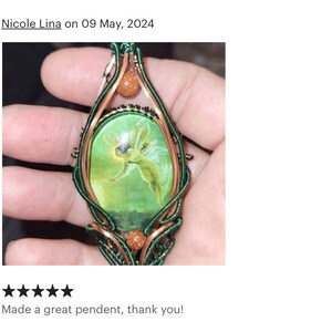 Op de afbeelding: Een hanger van groen en koperdraad met een groene cameo met een fee-afbeelding. De cameo is omgeven door koperdraad en geaccentueerd met kleine, ronde, oranje-bruine stenen.