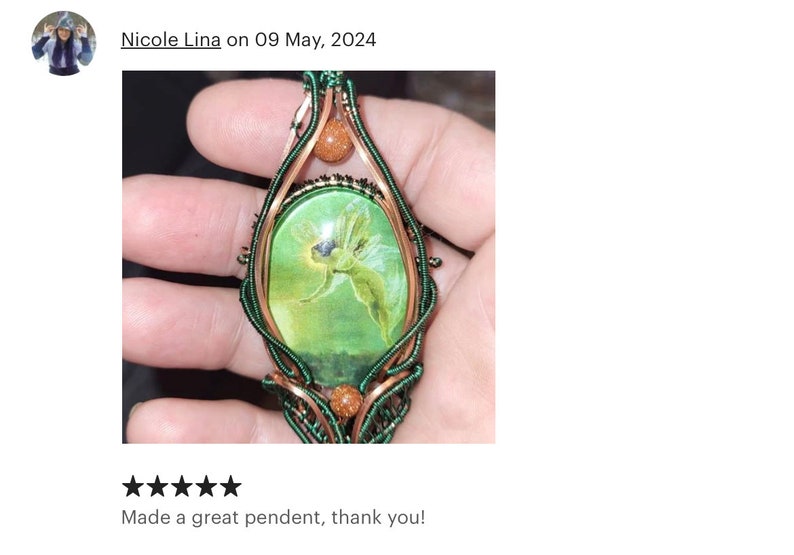 Op de afbeelding: Een hanger van groen en koperdraad met een groene cameo met een fee-afbeelding. De cameo is omgeven door koperdraad en geaccentueerd met kleine, ronde, oranje-bruine stenen.