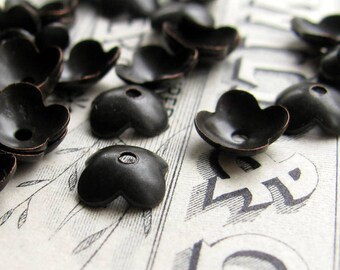 May include: A collection of black metal flower-shaped embellishments with a copper-toned finish. The embellishments have five petals and a small hole in the center.