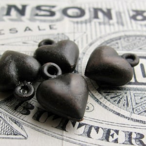 May include: Four black metal heart-shaped charms with a shiny finish. The charms have a loop at the top for attaching to a necklace or bracelet.