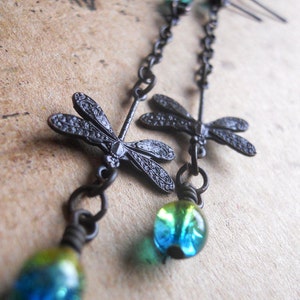 May include: Black dangle earrings with two dragonfly charms and a blue and green glass bead at the bottom.