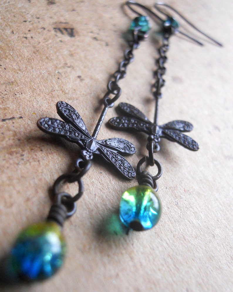 May include: Black dangle earrings with two dragonfly charms and a blue and green glass bead at the bottom.