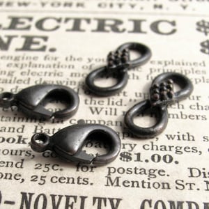 May include: Four antique silver-toned metal charms. Two are infinity symbols with small beads. Two are lobster claw clasps.