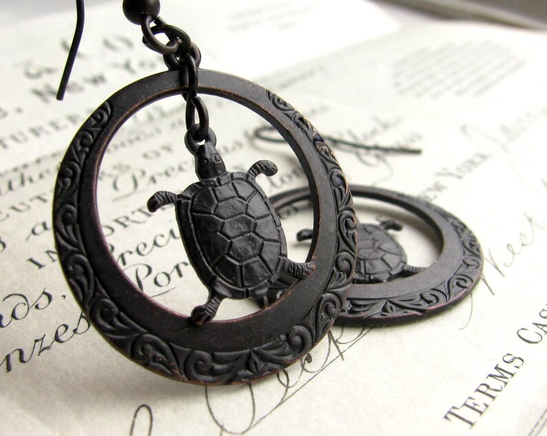 May include: A pair of black oxidized silver earrings with a detailed floral design. Each earring features a small turtle charm hanging from the center.