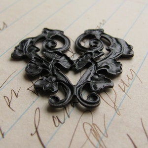 May include: Black metal heart-shaped decorative embellishment with a floral design. The embellishment is on a sheet of lined paper.