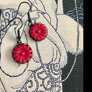 May include: A pair of dangle earrings with red flower-shaped glass beads and black metal accents.