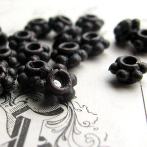 May include: A close-up of a group of black metal beads with a flower-like design. The beads have a slightly aged, antique look.