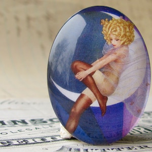 May include: A round glass cabochon featuring a vintage illustration of a woman in a white dress seated on a crescent moon. The background is a blue and purple gradient.