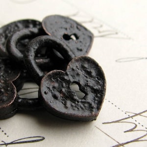 May include: Heart-shaped metal lock charms in a dark bronze color. The black charms have a textured surface and a keyhole in the center.