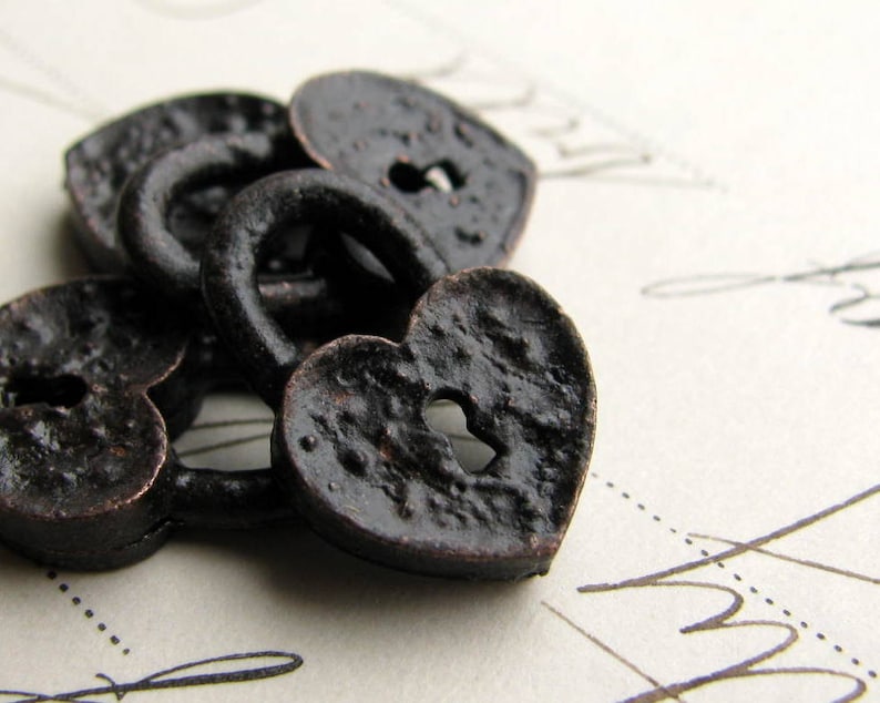 May include: Heart-shaped metal lock charms in a dark bronze color. The black charms have a textured surface and a keyhole in the center.