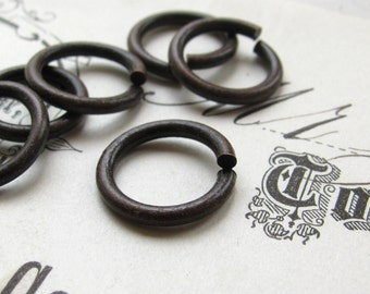 May include: Close-up of several small, dark brown metal rings. The rings are circular with a small opening, suggesting they are jump rings. The rings have a rustic, aged appearance, and are likely used for jewelry making or crafts.