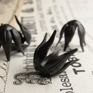 May include: Three black plastic flower-shaped embellishments. The embellishments have a pointed, petal-like design.