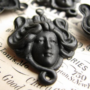 May include: Black resin cameo featuring a woman's face with elaborate hair. The cameo is a decorative embellishment with a loop for hanging.