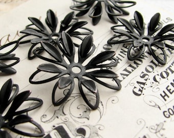 May include: A collection of matte black metal flower-shaped findings, each featuring a central circular hole and multiple radiating petals. These components are arranged in a cluster, showcasing a dark finish and a delicate, open-work design.