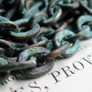 K&ouml;nnte beinhalten: Nahaufnahme einer Kette aus Metallgliedern mit einer dunkelgr&uuml;nen Patina. Die Kette liegt auf einem St&uuml;ck Papier mit dem aufgedruckten Wort "PROVIS".