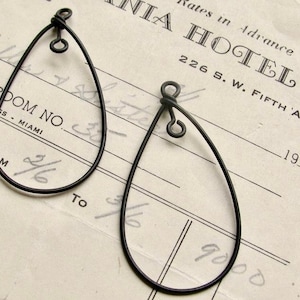 May include: Two black wire earrings shaped like teardrops. The earrings are hanging from a white piece of paper with black text.