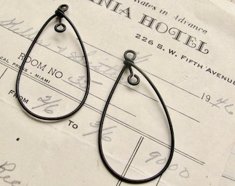 May include: Two black wire earrings shaped like teardrops. The earrings are hanging from a white piece of paper with black text.