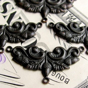 May include: Several antique bronze-colored metal embellishments with ornate, symmetrical designs. Each piece features swirling patterns, acorn-like details, and small loops for attachment, suggesting use in jewelry or craft projects.