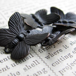 May include: Five black metal butterfly charms with a detailed design. The charms have a loop on the top for attaching to jewelry or other crafts.