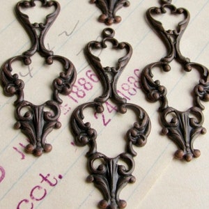 May include: Five antique bronze metal charms with intricate filigree designs. Each charm features a heart-shaped center with ornate scrollwork and a loop at the top for hanging.