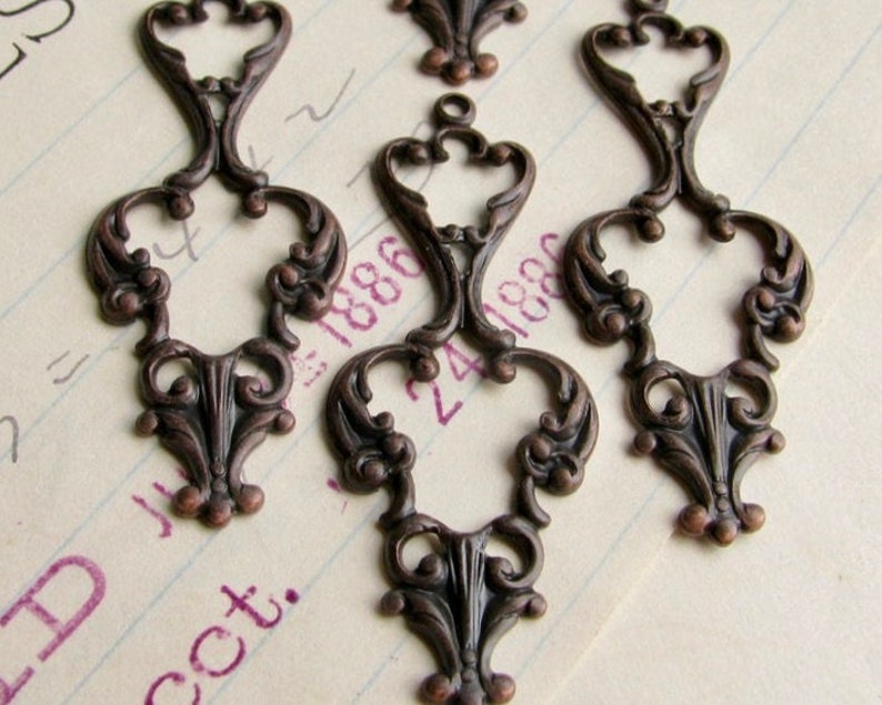 May include: Five antique bronze metal charms with intricate filigree designs. Each charm features a heart-shaped center with ornate scrollwork and a loop at the top for hanging.