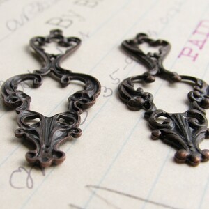May include: Two ornate metal embellishments with a decorative, scroll-like design. The embellishments are a dark bronze color and have a vintage look.