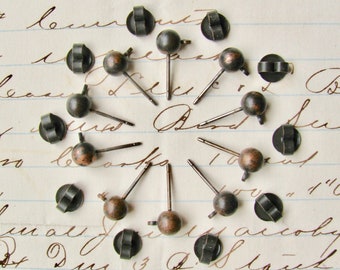 May include: A collection of 16 bronze-colored earring studs with black metal backs. The studs are arranged in a circle on a sheet of lined paper.