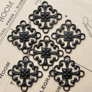 May include: Six black metal decorative charms with a cross design. Each charm is square shaped with intricate details and a small flower in the centre.