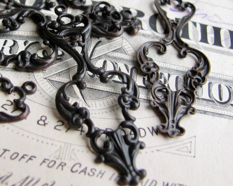 May include: A collection of ornate, black metal embellishments with intricate scrollwork designs. These decorative pieces are perfect for adding a touch of vintage charm to crafts, jewelry, or home decor.