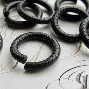 Puede incluir: Un conjunto de anillos de metal negro con un acabado texturizado. Los anillos son todos del mismo tama&ntilde;o y est&aacute;n dispuestos en una pila.