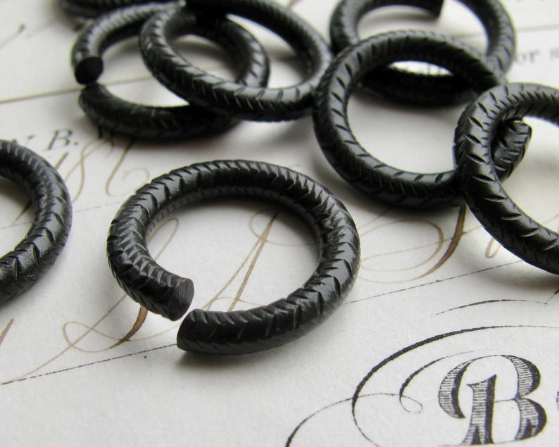 Puede incluir: Un conjunto de anillos de metal negro con un acabado texturizado. Los anillos son todos del mismo tama&ntilde;o y est&aacute;n dispuestos en una pila.