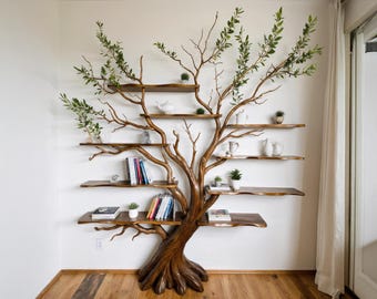 May include: A unique, tree-shaped bookshelf made of brown wood, mounted on a white wall. The shelves hold books, small plants, and decorative items. Green leaves and branches extend from the top, adding a natural aesthetic to the room.