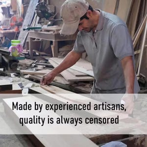 May include: A carpenter in a workshop is measuring a piece of wood. The image includes the text "Made by experienced artisans, quality is always censored". The artisan is wearing a gray shirt and a cap. The workshop has various tools and wood pieces.
