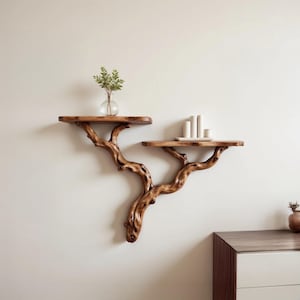 Könnte beinhalten: Zwei Holzregale in Form von Baumästen, die an einer weißen Wand montiert sind. Das obere Regal hat eine kleine Glasvase mit grünen Blättern. Das untere Regal hat ein kleines weißes rechteckiges Tablett mit drei weißen Keramikobjekten.