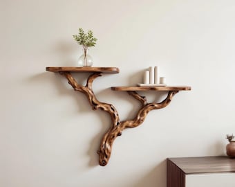 May include: Two wooden shelves shaped like tree branches mounted on a white wall. The top shelf has a small glass vase with green leaves. The bottom shelf has a small white rectangular tray with three white ceramic objects.