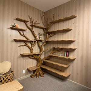 Könnte beinhalten: Ein einzigartiges, handgefertigtes Bücherregal in Form eines Baumes aus Holz. Das Bücherregal ist als Baum gestaltet und verfügt über mehrere Regale unterschiedlicher Größe. Der Baum ist in einem warmen Braunton gehalten, die Regale in einem helleren Braun. Ein dekoratives Element.