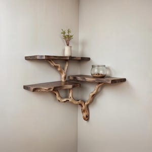 Könnte beinhalten: Ein Satz aus drei Holzregalen mit einem natürlichen Astdesign. Die Regale sind in einer Ecke montiert und aus dunklem Holz mit einer natürlichen Oberfläche gefertigt. Die Regale sind leer, aber auf dem oberen Regal steht eine kleine Pflanze in einem weißen Topf und auf dem mittleren Regal befindet sich ein Glasgefäß mit kleinen Gegenständen.