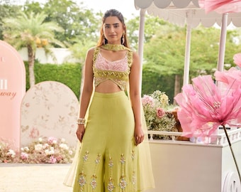 May include: A lime green two-piece outfit with intricate embroidery. The top is a crop top with a pink bodice and a cutout. The pants are wide-legged with detailed embroidery. The outfit is accessorized with a matching choker and bracelet.