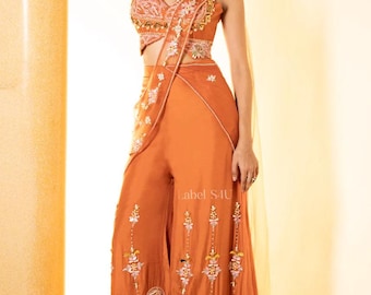 May include: An orange embroidered palazzo pantsuit. The sleeveless crop top and wide-leg pants are adorned with intricate floral embroidery. A matching draped scarf and belt complete the ensemble. The text "label S4U" is visible on the pants.