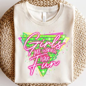 May include: A white t-shirt with a neon green and pink graphic design that says "Girls just wanna have fun" in a retro style.